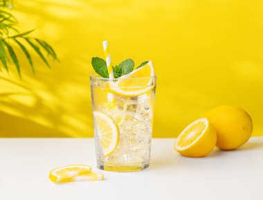 Palmiye yaprağı ve narenciye meyveleriyle sarı ve beyaz arka planda limonata, nane ve buzlu soğuk limonata. Sıcak bir yaz gününde ferahlatıcı ve sağlıklı bir içecek konsepti..