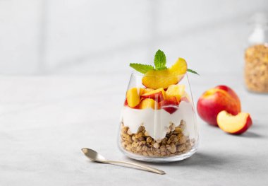 Şeftalili yoğurt parfe ve taze meyveli hafif bir arka planda bir bardakta granola. Sağlıklı beslenme konsepti. Besleyici bir yaz kahvaltısı. Boşluğu kopyala.
