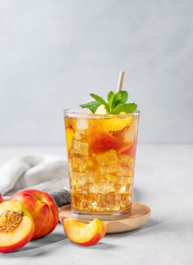 Şeftalili buzlu nane çayı. Sağlıklı ev yapımı soğuk yaz içeceği kavramı, arka planda hafif meyve ve gölgeli uzun bir bardakta. Ön görünüm ve boşluk kopyala.
