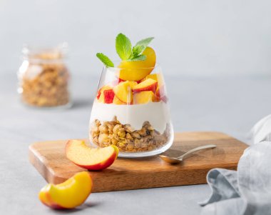 Şeftalili Yunan yoğurdu ve tahtadan bir tahtanın üzerinde taze meyve ve peçeteyle yapılmış bir bardakta granola. Sağlıklı beslenme konsepti. Besleyici yaz kahvaltısı. 