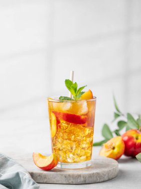 Misket tahtasında şeftalili buzlu nane çayı. Sağlıklı ev yapımı soğuk yaz içeceği kavramı, arka planda hafif meyve ve gölgeli uzun bir bardakta. Ön görünüm ve boşluk kopyala.