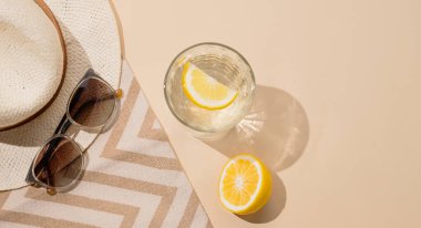 Limonata, taze narenciye meyveleri, bej arka planda plaj havlusunda şapka ve güneş gözlüğü. Sağlıklı içeceklerle yaz tatili konsepti. Üst görünüm ve kopyalama alanı.
