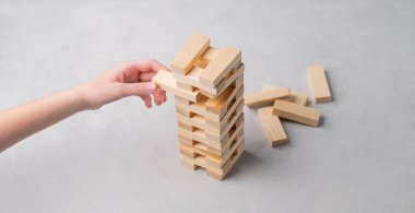 Bir el, arka plandaki ahşap bir kuleden bir parça çıkarır. Aile entellektüel oyunu Jenga kavramı. 
