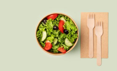 Yeşil arka planda ahşap çatallı kağıt bir kabın içinde domatesli taze yeşil salata ve salatalık. Biyolojik olarak ayrıştırılabilir çevre dostu paket servis yemeklerinde sağlıklı gıda konsepti. Üst görünüm ve kopyalama alanı