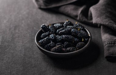 Siyah ahşap kasede yaprak ve peçeteyle kaplanmış taze siyah dut. Sulu ve sağlıklı mevsimlik bahçe meyveleri kavramı. Boşluğu kopyala. 