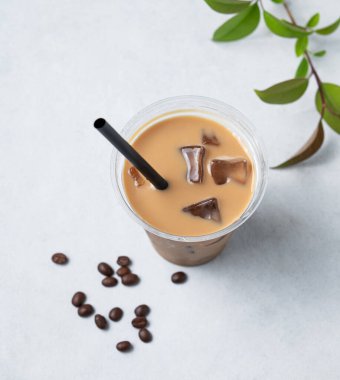 Geri dönüşümlü plastik bardakta buzlu kahve, kahve çekirdekleri ve yapraklı hafif bir arka planda süt ve buz. Soğuk yaz içkisi konsepti. Üst görünüm. 