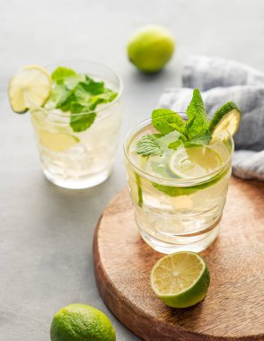 İki bardak naneli limonlu mojito ve tahta tahtada buz. Hafif bir arka planda narenciye kokteyli tazeleniyor. Yaz soğuk limonata içecekleri konsepti. 