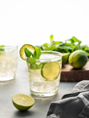 Naneli ve buzlu iki bardak limonlu mojito. Hafif bir arka planda narenciye kokteyli tazeleniyor. Yaz soğuk limonata içkisi konsepti. Ön görünüm.