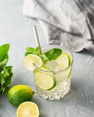 Mojito taze limonla içilir. Narenciye, nane ve buzlu, gri arka planda bitki ve peçeteyle taze bir kokteyl. Soğuk limonata konsepti. Üst görünüm.