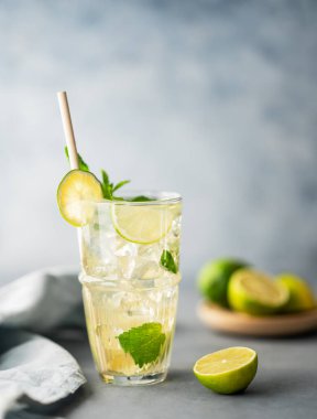 Limonlu, naneli ve buzlu uzun bardakta mojito kokteyli ve peçeteli mavi desenli bir arka plan. Turunçgil meyveleriyle ferahlatıcı limonata içeceği konsepti. Boşluğu kopyala. 