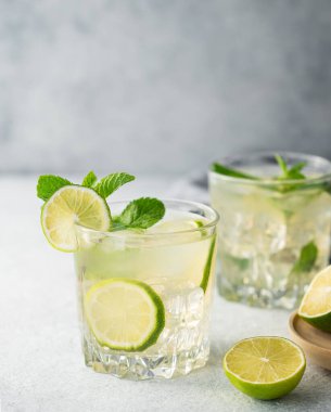 Açık mavi arka planda iki bardak mojito kokteyli, limon, nane ve buz. Turunçgil meyveli limonata konsepti.