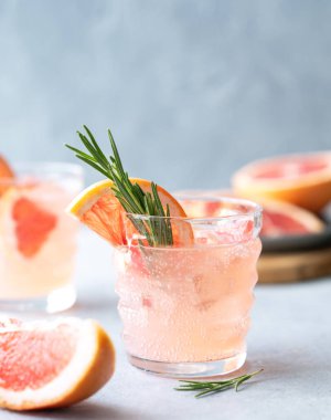 İki bardak greyfurtlu limonata, biberiyeli ve mavi arka planda buz ve taze narenciye dilimleri. Moda, yaz, sağlıklı ve ferahlatıcı kokteyl konsepti. Ön görünüm.