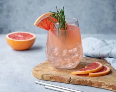 Biberiyeli ev yapımı greyfurt limonatası ve taze narenciye dilimleri ve peçeteyle mavi arka planda ahşap bir tahtanın üzerinde buz. Moda, yaz içkisi konsepti. Ön görünüm.