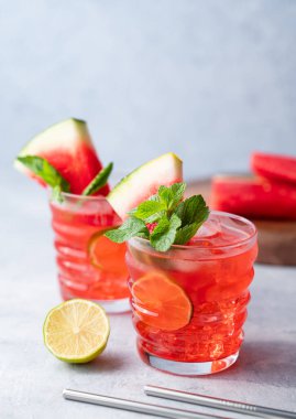İki bardak karpuz kokteyli. Limonlu, buzlu ve naneli. Mavi arka planda, meyveli. Havalı yaz ferahlatıcı limonata içeceği konsepti. Ön görünüm.