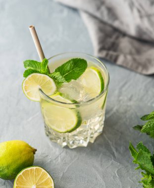 Mojito taze limonla içilir. Narenciye, nane ve buzlu kokteyl ve gri arka planda bitki ve peçeteyle yakın plan. Soğuk limonata konsepti. Üst görünüm.