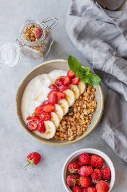 Müsli, çilek ve muzlu Yunan yoğurdu taze böğürtlen, granola ve peçeteyle mavi bir zemin üzerinde. Sağlıklı, doğal ve besleyici kahvaltı kavramı. Üst görünüm.