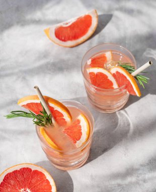 Biberiye ve buzlu greyfurt mojito kokteyli. Hafif arka planda iki bardak, taze narenciye ve gölgeyle birlikte. Moda, yaz, sağlıklı ve ferahlatıcı limonata içeceği.. 