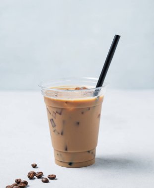 Geri dönüşümlü plastik bardakta buzlu kahve, kahve çekirdekleri ve hafif bir arka planda süt ve buz. Soğuk yaz içkisi konsepti. Ön görünüm ve boşluk kopyala. 