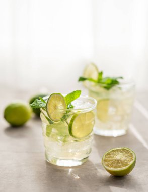 İki bardak nane ve buzlu limonata. Mojito kokteylini limonlu arka plan ve sabah ışığıyla tazeliyorum. Yaz soğuk içecekler konsepti. Boşluğu kopyala.