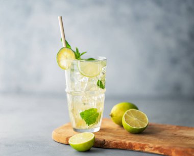 Uzun bardakta mojito kokteyli, kireç, nane ve buzlu mavi desenli arka planda ahşap bir tahta üzerinde. Turunçgil meyveleriyle ferahlatıcı limonata içeceği konsepti. Boşluğu kopyala. 