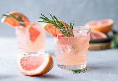 İki bardak greyfurtlu limonata, biberiyeli ve mavi arka planda buzlu taze narenciye meyveli. Moda, yaz, sağlıklı ve ferahlatıcı kokteyl konsepti. Ön görünüm.