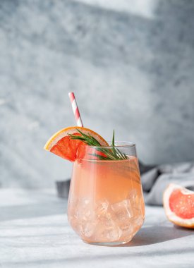 Biberiyeli greyfurt limonatası ve mavi arkaplanda buzlu taze narenciye dilimleri ve gölgesi olan bir bardak. Moda, yaz, sağlıklı ve ferahlatıcı kokteyl konsepti. Ön görünüm.