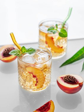 Beyaz arka planda buzlu ve naneli ev yapımı şeftalili limonata. Bardakta taze buzlu çay ve pencereden gelen ışık. Bar veya kafe menüsü için yaz içeceği tarifi konsepti tazeleniyor.