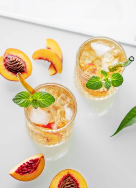 Beyaz arka planda buzlu ve naneli ev yapımı şeftalili limonata. Bardakta taze buzlu çay ve pencereden gelen ışık. Bar ya da kafe menüsü için yaz içeceği tarifi konseptini tazeliyorum. Üst görünüm