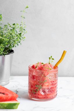 Taze bitkiler ve meyvelerle beyaz mermer zemin üzerinde kekik ve buzla karpuz kokteylini tazeliyorum. Sağlıklı yaz içeceği ya da kafe ya da bar menüsü için limonata. Ön görünüm.