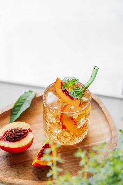 Şeftalili limonata, buzlu ve nane şekerli beyaz bir masada tahta bir tahta üzerinde. Taze buzlu çay ve camdan gelen ışık. Bar ya da kafe menüsü için yaz içeceği tarifi konseptini tazeliyorum. Üst görünüm