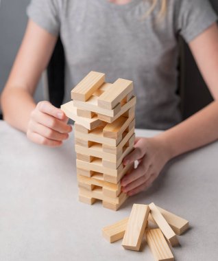 Bir çocuk bir masada oturuyor ve eli bir tahta kule oyunundan hafif arka planda bir parça çıkarıyor. Aile entellektüel oyunu kavramı.