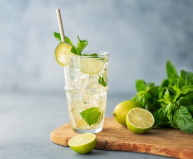 Uzun bardakta mojito kokteyli, kireç, nane ve buzla birlikte ahşap bir tahta üzerinde taze bitkiyle mavi desenli bir arka planda. Turunçgil meyveleriyle ferahlatıcı limonata içeceği konsepti. Boşluğu kopyala