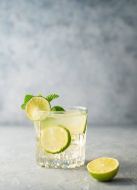 Mojito kokteyli ve arka planda taze limon. Turunçgiller, nane ve buzla yaz ferahlatıcı içecek konsepti. Ön görünüm ve boşluk kopyala..