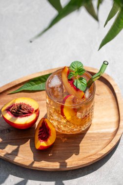 Buzlu şeftali ve naneli limonata. Beton zemin üzerinde tahta bir tahta üzerinde. Gölgeli ve palmiye yapraklı taze buzlu çay. Bar veya kafe menüsü için yaz içeceği tarifi konsepti tazeleniyor. 