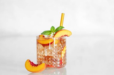 Şeftali ferahlatıcı içecek buzlu ve beyaz bir masada nane şekeri. Bardakta taze ev yapımı limonata. Bar veya kafe menüsü için yaz buzlu çay tarifi konsepti. Ön görünüm ve boşluk kopyala.