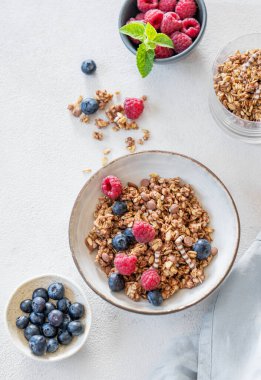 Tahıl gevreği, ahududu ve yaban mersinini taze böğürtlen ve sabah güneşiyle birlikte hafif bir arka planda bir kaseye koydum. Sağlıklı ve besleyici kahvaltı konsepti. Üst görünüm.
