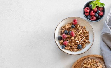 Müsli ya da granola, ahududu ve yabanmersini arkaplanda taze böğürtlen ve sabah güneşi olan bir kasede. Sağlıklı ve besleyici kahvaltı konsepti. Üst görünüm ve kopyalama alanı.