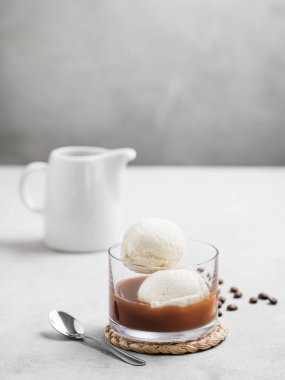 Vanilyalı dondurma kepçeli Affogato kahvesi ve kahve çekirdeği ve kaşıkla hafif arka planda bir bardakta espresso. Klasik İtalyan tatlı konsepti. Ön görünüm ve boşluk kopyala.