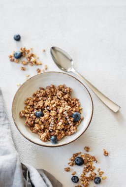 Hafif arka planda yaban mersinli granola taze böğürtlen, kaşık ve sabah güneşiyle birlikte. Sağlıklı ve besleyici kahvaltı konsepti. Üst görünüm ve kopyalama alanı.