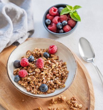 Müsli ya da granola, ahududu ve yaban mersini, ahşap bir kasede hafif bir arka planda taze böğürtlen, kaşık ve sabah güneşiyle birlikte. Sağlıklı ve besleyici kahvaltı konsepti. Üst görünüm.