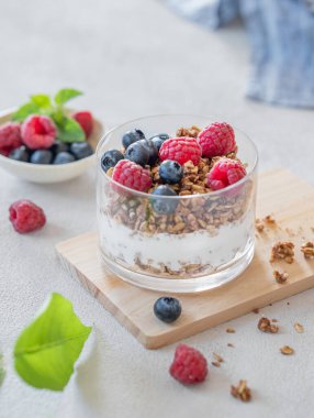 Doğal Yunan yoğurdu, granola, ahududu ve böğürtlen. Arka planda hafif bir bardakta, taze böğürtlen ve sabah güneşiyle. Sağlıklı ve besleyici kahvaltı konsepti. 