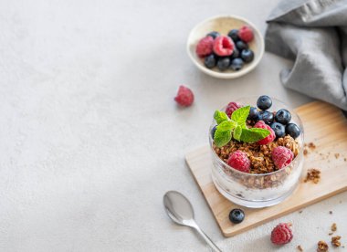 Mısır gevreği, ahududu ve böğürtlenli Yunan yoğurdu taze böğürtlen ve sabah güneşiyle birlikte arka planda ahşap bir tahtanın üzerinde bir bardakta. Sağlıklı ve besleyici kahvaltı konsepti. Üst görünüm