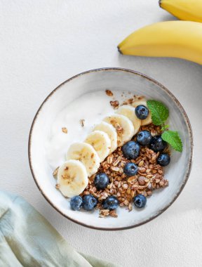 Yoğurtlu, muzlu ve yaban mersinli granola. Arka planda hafif bir arka planda. Süt ürünleri, müsli ve taze meyvelerden sağlıklı kahvaltı kavramı. Üst görünüm.