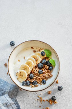 Mısır gevreği ya da müsli ile doğal yoğurt, muz ve yaban mersinleri beyaz arka planda bir kasede sabah ışığında taze böğürtlen. Sağlıklı ve besleyici kahvaltı konsepti. Üst görünüm ve kopyalama alanı