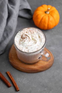 Süslü balkabağı ve tarçın çubuğuyla ahşap zemin üzerinde cam bardakta kremalı baharatlı latte. Moda sonbahar ılık içeceği kavramı. Üst görünüm ve kopyalama alanı.