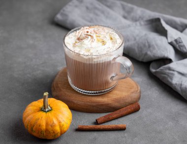 Süslü balkabağı ve tarçın çubuğuyla ahşap zemin üzerinde cam bardakta kremalı baharatlı latte. Moda sonbahar ılık içeceği kavramı. Boşluğu kopyala.