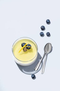 Mavi arka planda mavi bir arka planda böğürtlenli limonlu panna cotta ve taze böğürtlen, kaşık ve gölge. Geleneksel İtalyan tatlı konsepti. Üst görünüm ve kopyalama alanı.