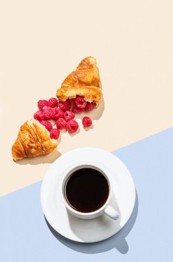 Bir fincan kahve ve kırık kruvasan ile sarı ve mavi arka planda taze ahududu. Kahvaltıda sağlıklı yiyecek ya da hamur işi için yaratıcı bir model ve konsept. Üst görünüm ve kopyalama alanı.