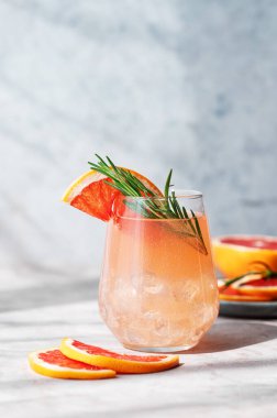 Biberiye ve buzlu greyfurt mojito, mavi arka planda taze narenciye dilimleri ve gölgesi olan bir bardakta. Moda, yaz, sağlıklı ve ferahlatıcı limonata ya da kokteyl konsepti. 