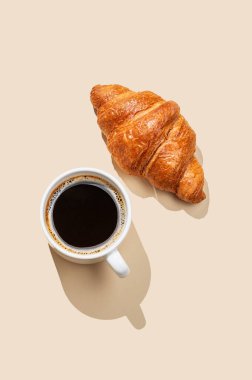 Kahve fincanı ve sarı arka planda taze kruvasan. Yaratıcı tasarım ve sağlıklı yemek ve Fransız kahvaltısı konsepti. Üst görünüm ve kopyalama alanı.